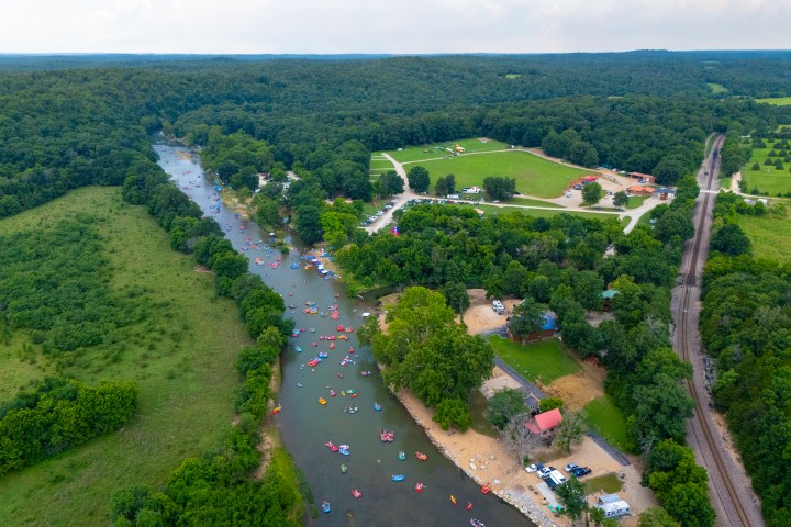 Aerial view of a river with people tubing, surrounded by lush greenery and a campground.