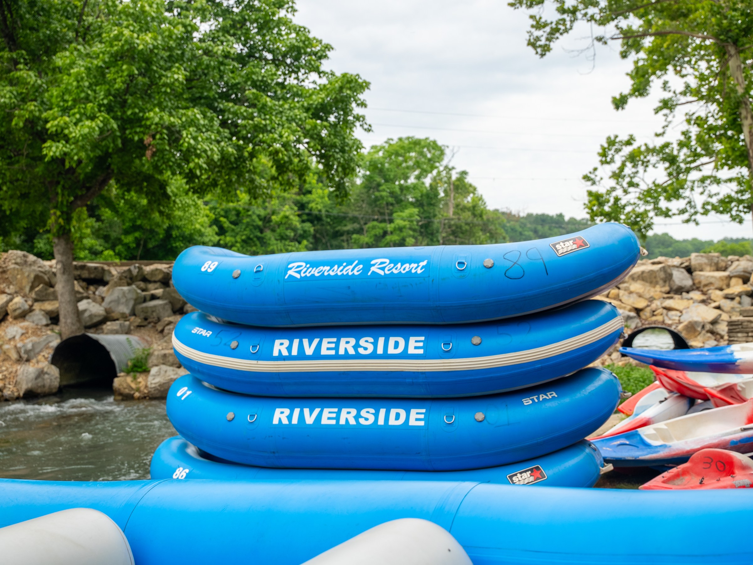 Stacked blue rafts labeled 'Riverside' near a river with trees.