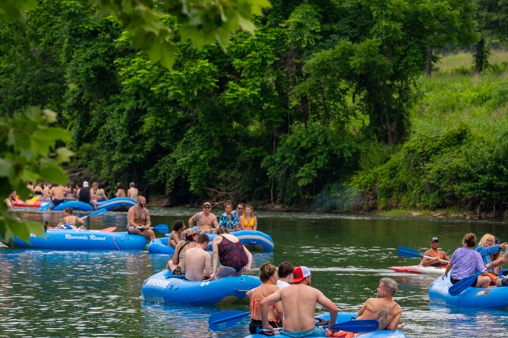 People relaxing on blue tubes floating down a tree-lined river.