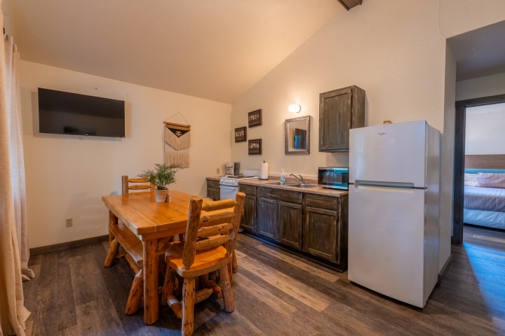 Rustic kitchen with wooden table, chairs, fridge, and wall decor.