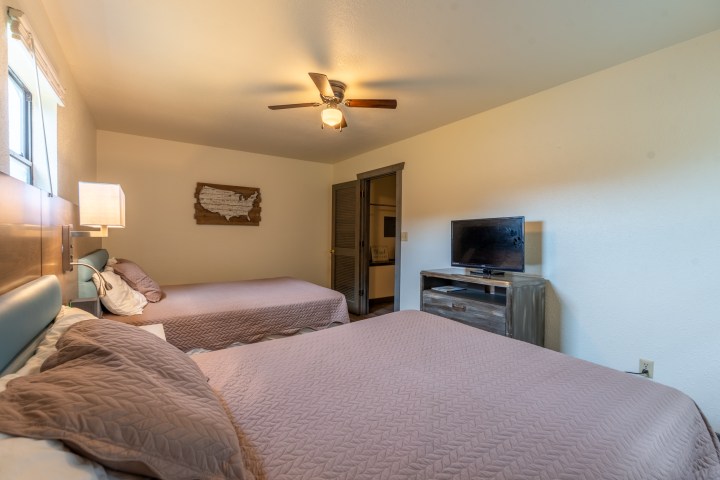 Room with two beds, TV, ceiling fan, and wall decor.