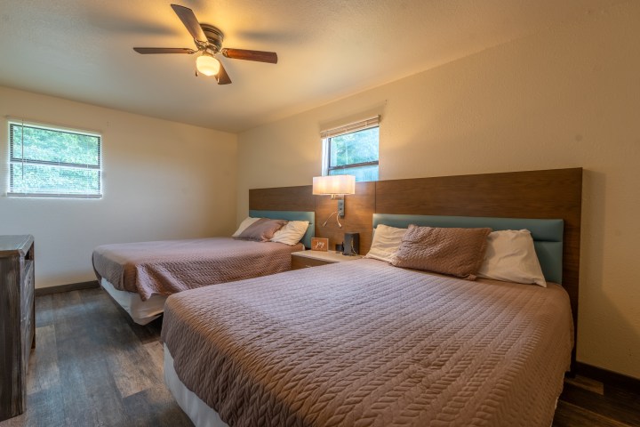 Room with two double beds, wooden headboards, and a ceiling fan.