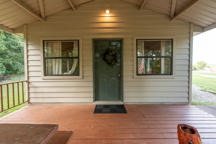 House porch with wooden floor, green door, and two windows with curtains.