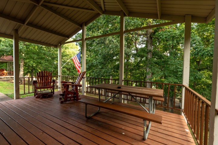 Covered wooden porch with picnic table, rocking chairs, and American flag.