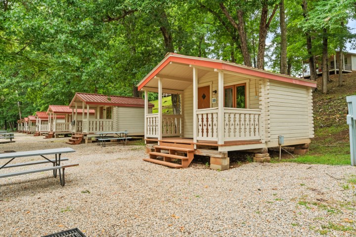 Row of small wooden cabins with porches in a wooded campground.