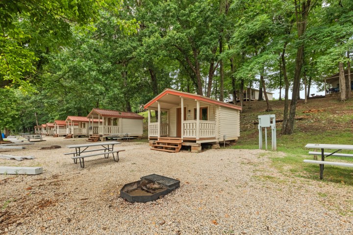 Row of small cabins and picnic tables surrounded by trees.