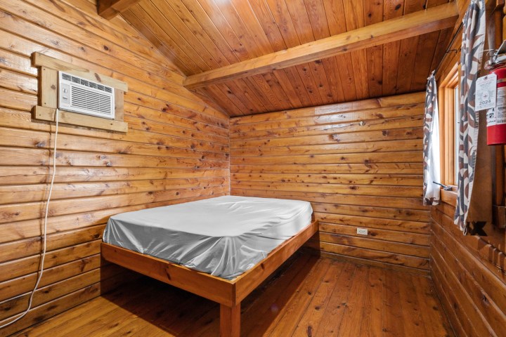 Wooden cabin room with a bed and air conditioner on wall.