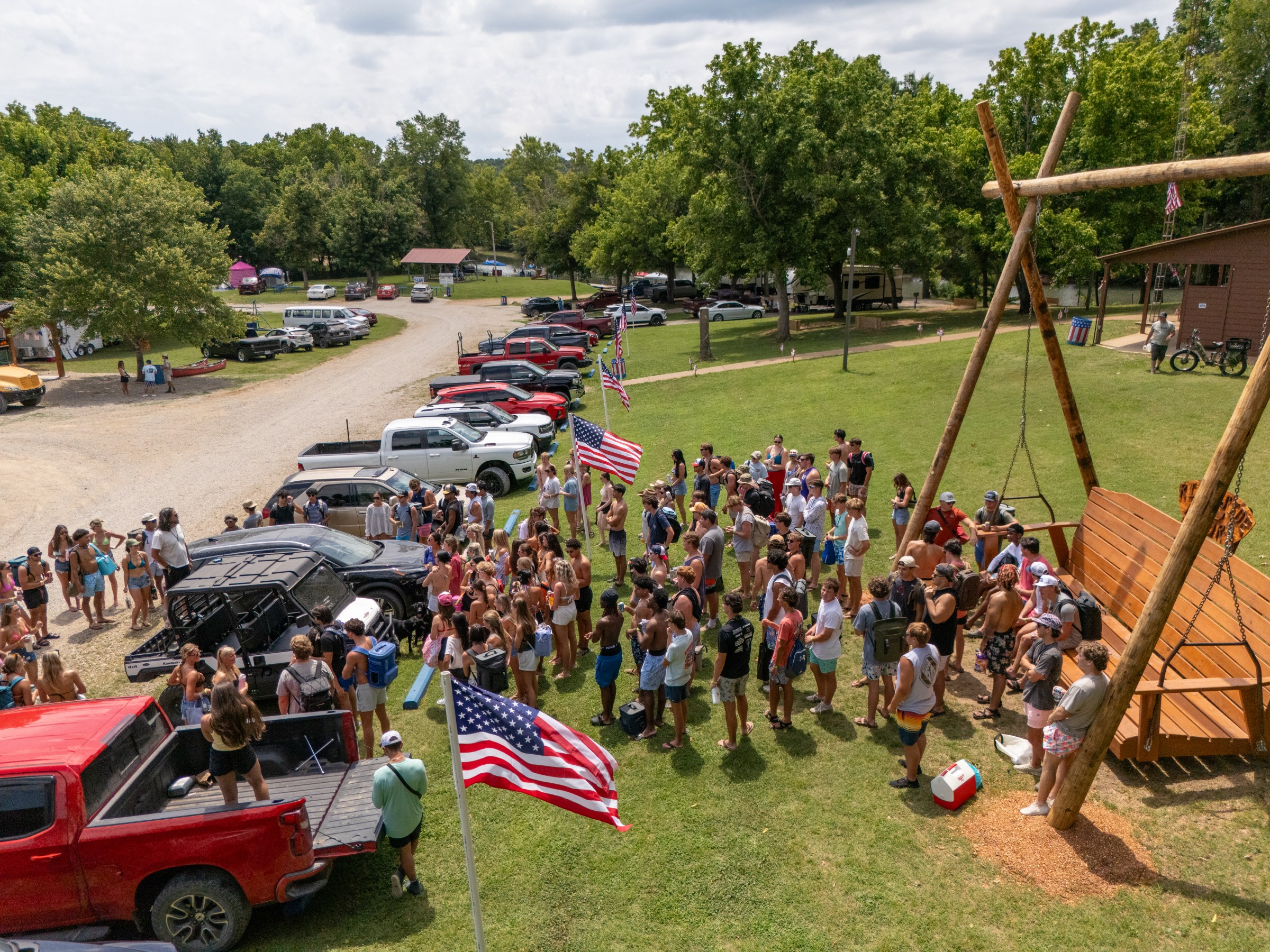 People gathering near vehicles and swing set outdoors, with American flags visible.