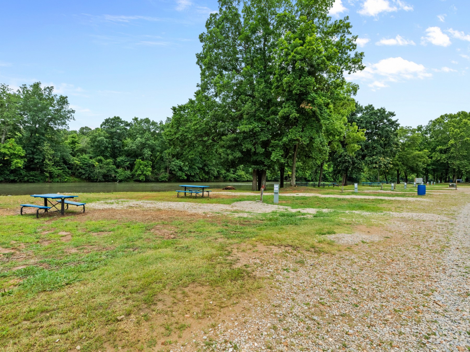 Park with picnic tables, trees, and a gravel path near a river.